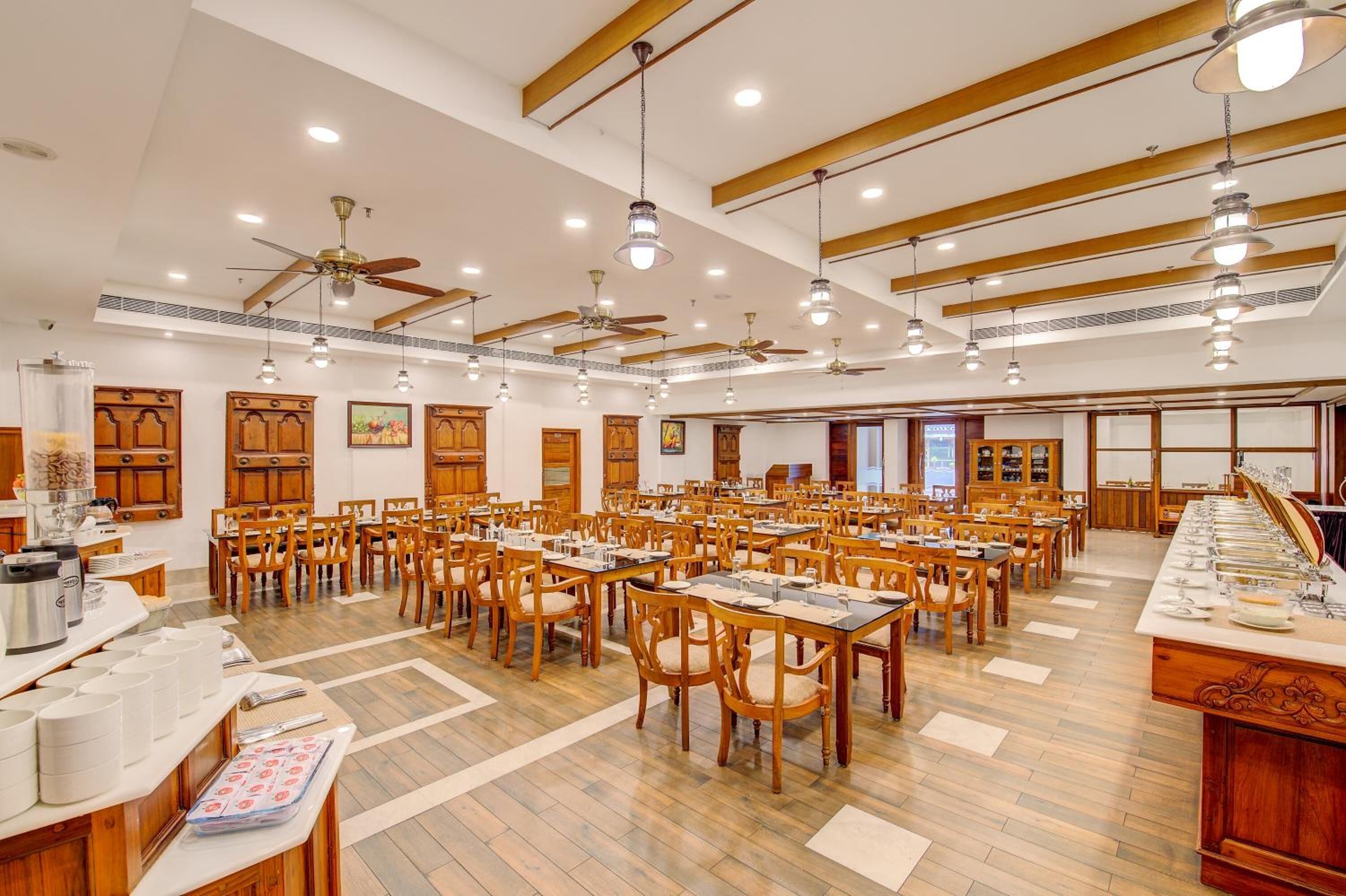 A large dining hall with multiple tables and chairs, ceiling fans, and pendant lighting.