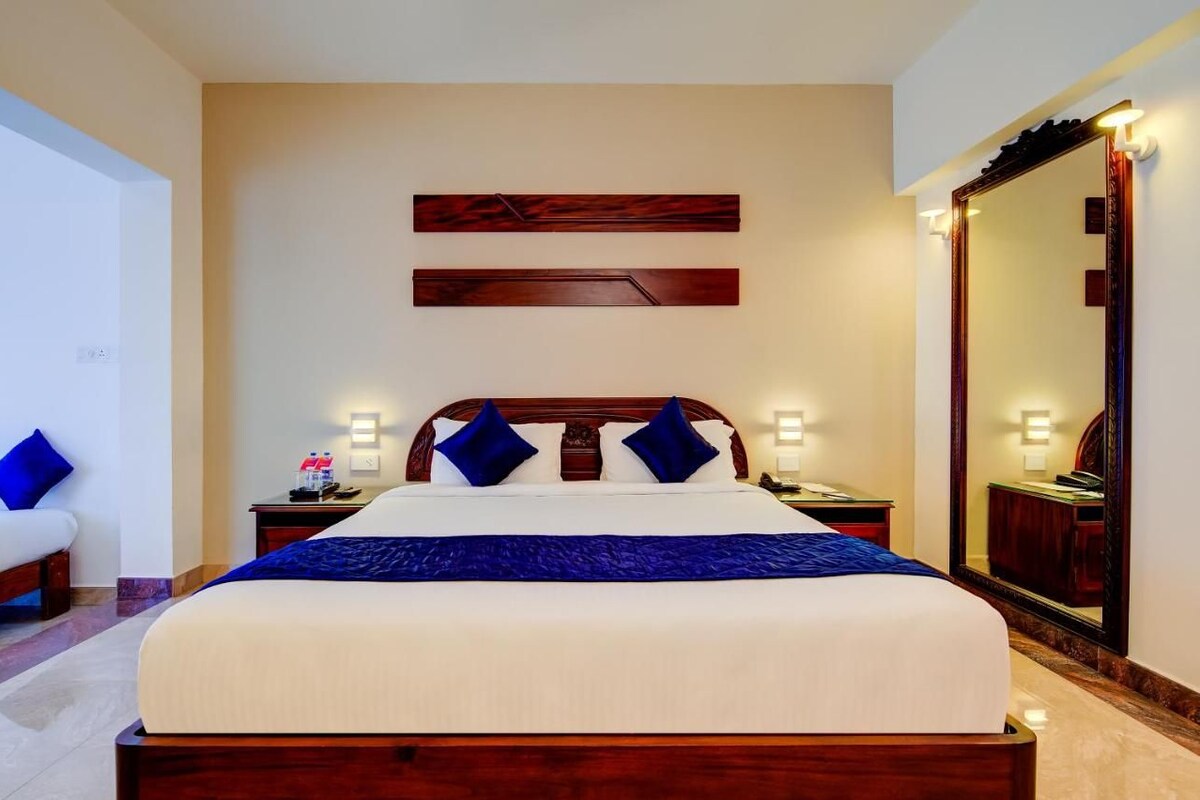 Habitación de hotel ordenada con una cama grande, mesitas de noche, un espejo y una obra de arte colgada en la pared.