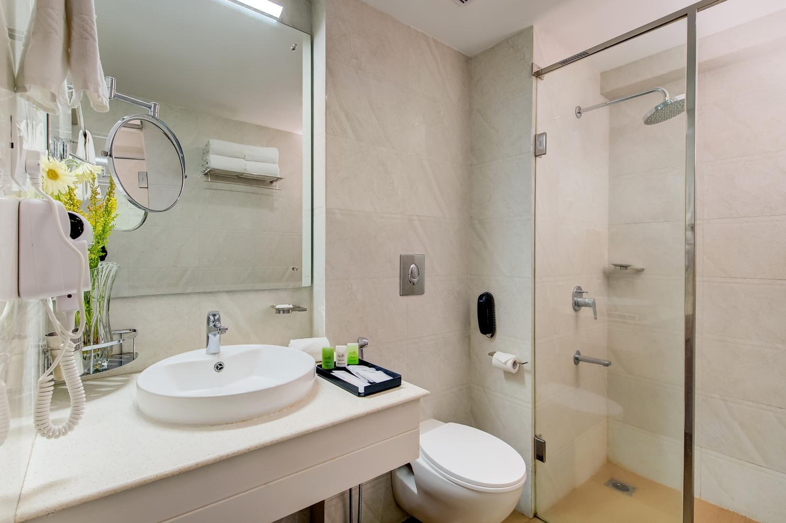 Een moderne badkamer met een wit wastafelmeubel, spiegel en toilet. Er is een douchecabine met glazen wanden en een handdoekhouder.
