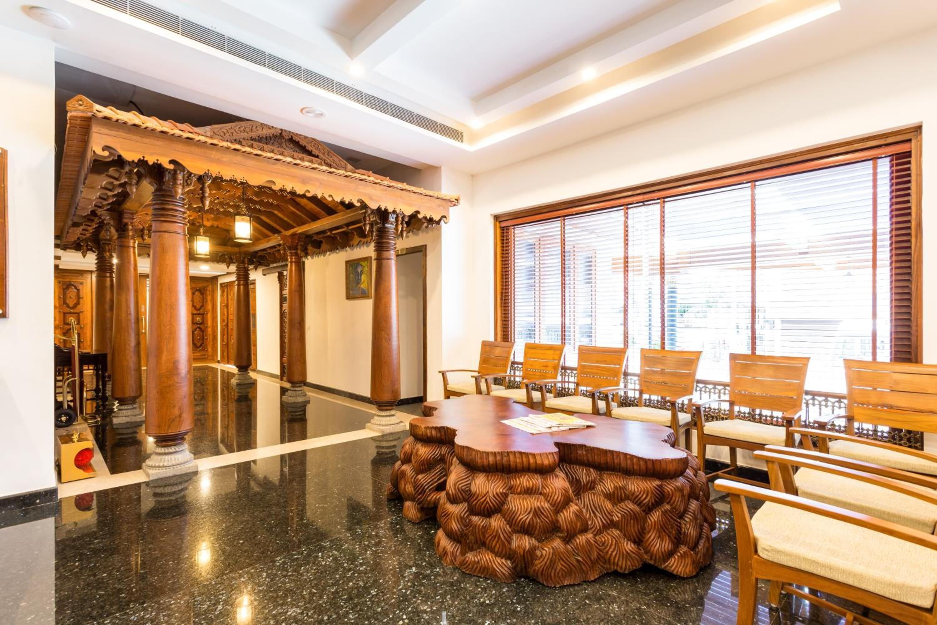 A lobby with a traditional wooden reception desk, a large window with blinds, and a polished marble floor.