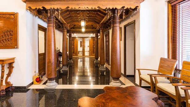 A hallway with wooden columns, a wooden bench, and a polished floor. - Sterling Guruvayur (Chavakkad)