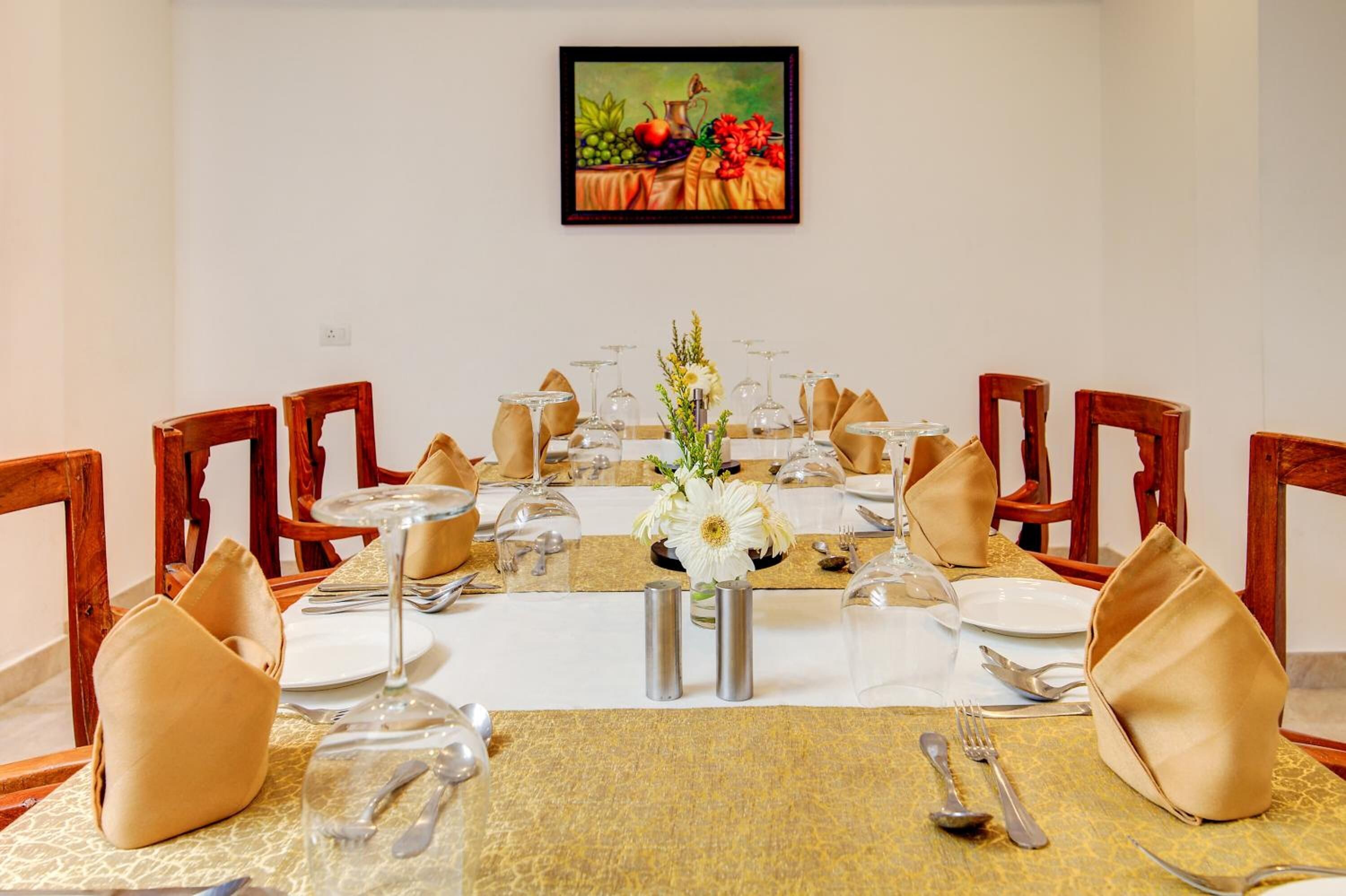A dining table set for a meal with chairs, a centerpiece, and a painting on the wall.