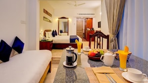 A hotel room with a bed, a dining table with breakfast items, a coffee maker, and a fruit bowl. - Sterling Guruvayur (Chavakkad)