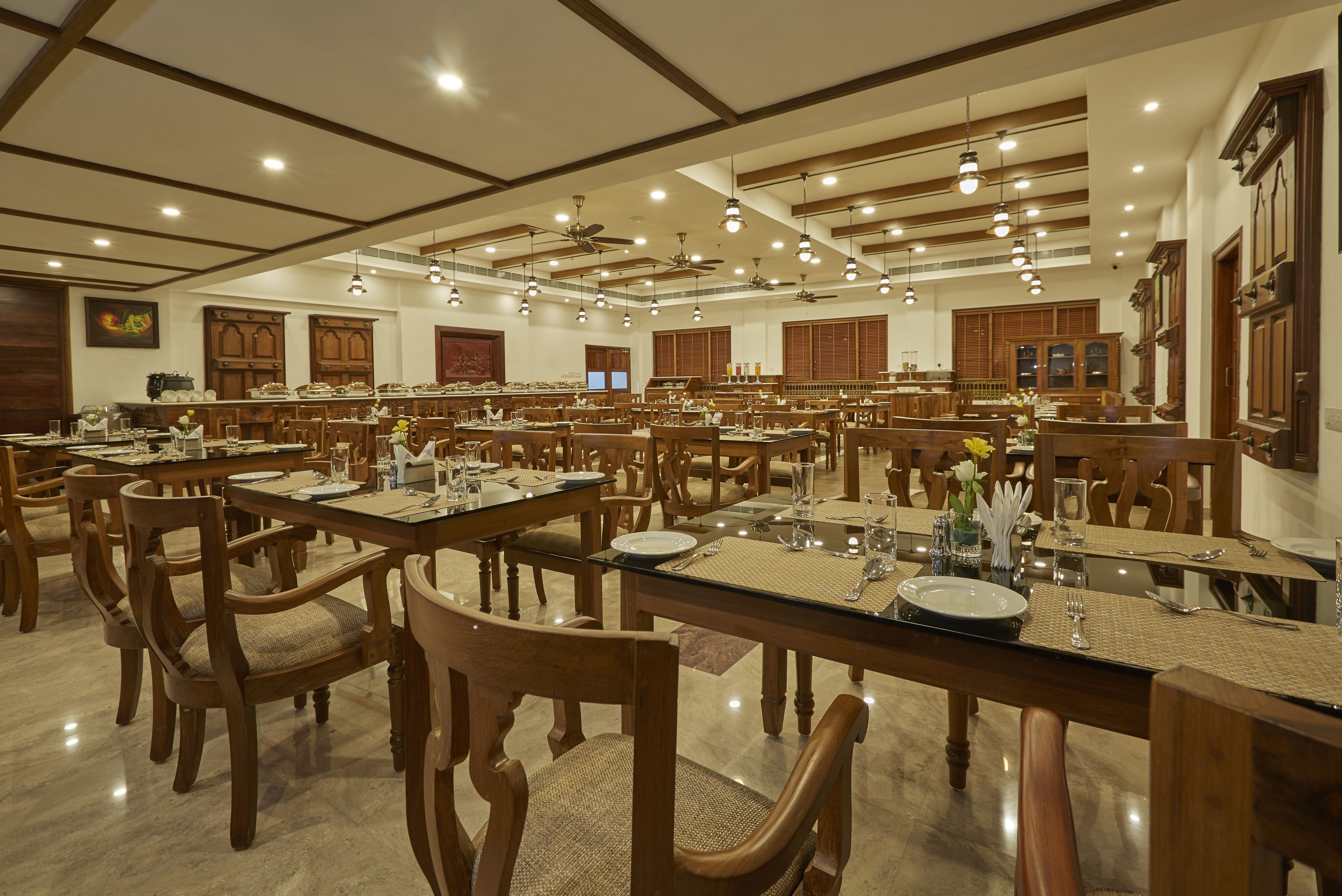 A spacious dining area with multiple tables and chairs, wooden cabinets, and ceiling fans.