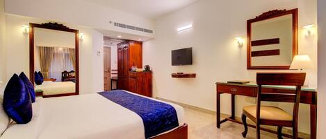 A hotel room with a large bed, a desk with a chair, a television, and a mirror.