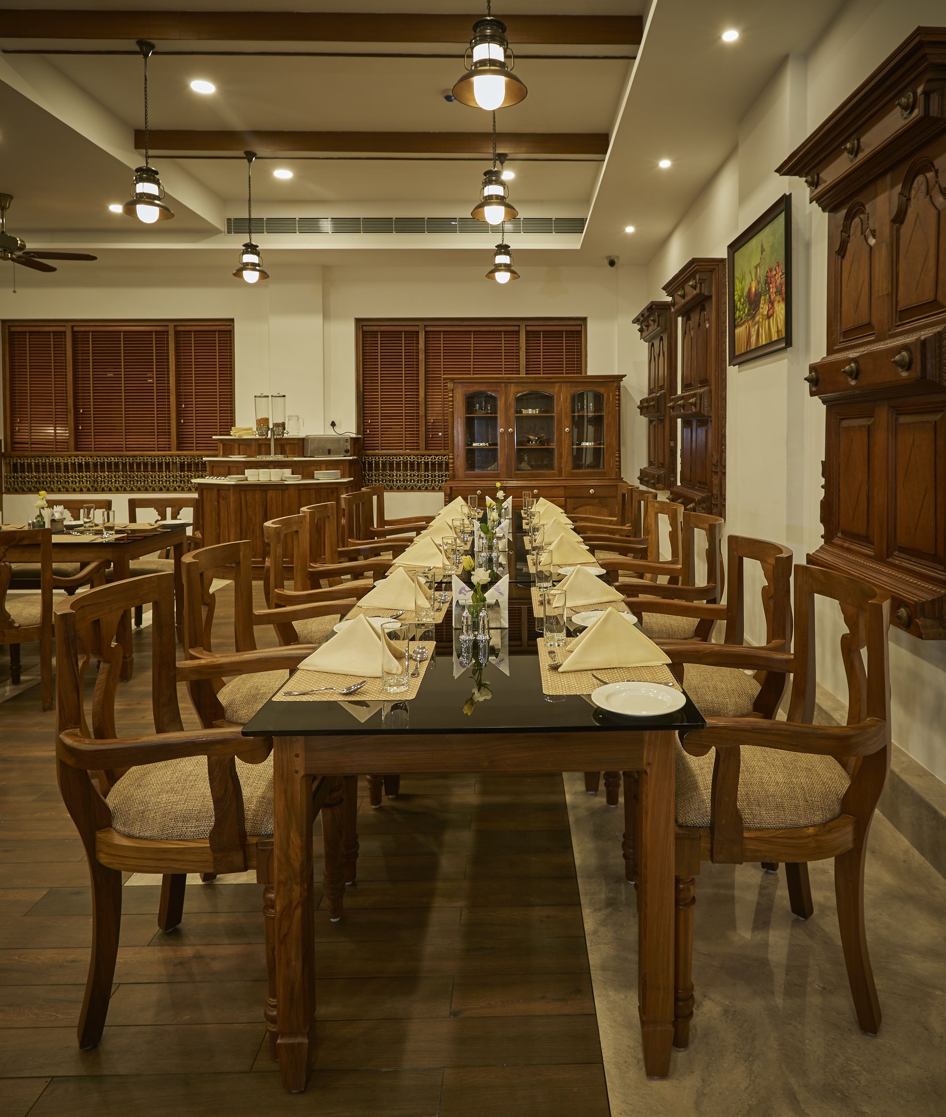 Une salle à manger élégante, avec de longues tables dressées pour accueillir de nombreux convives, des chaises en bois et, au fond, un buffet en bois de style traditionnel.