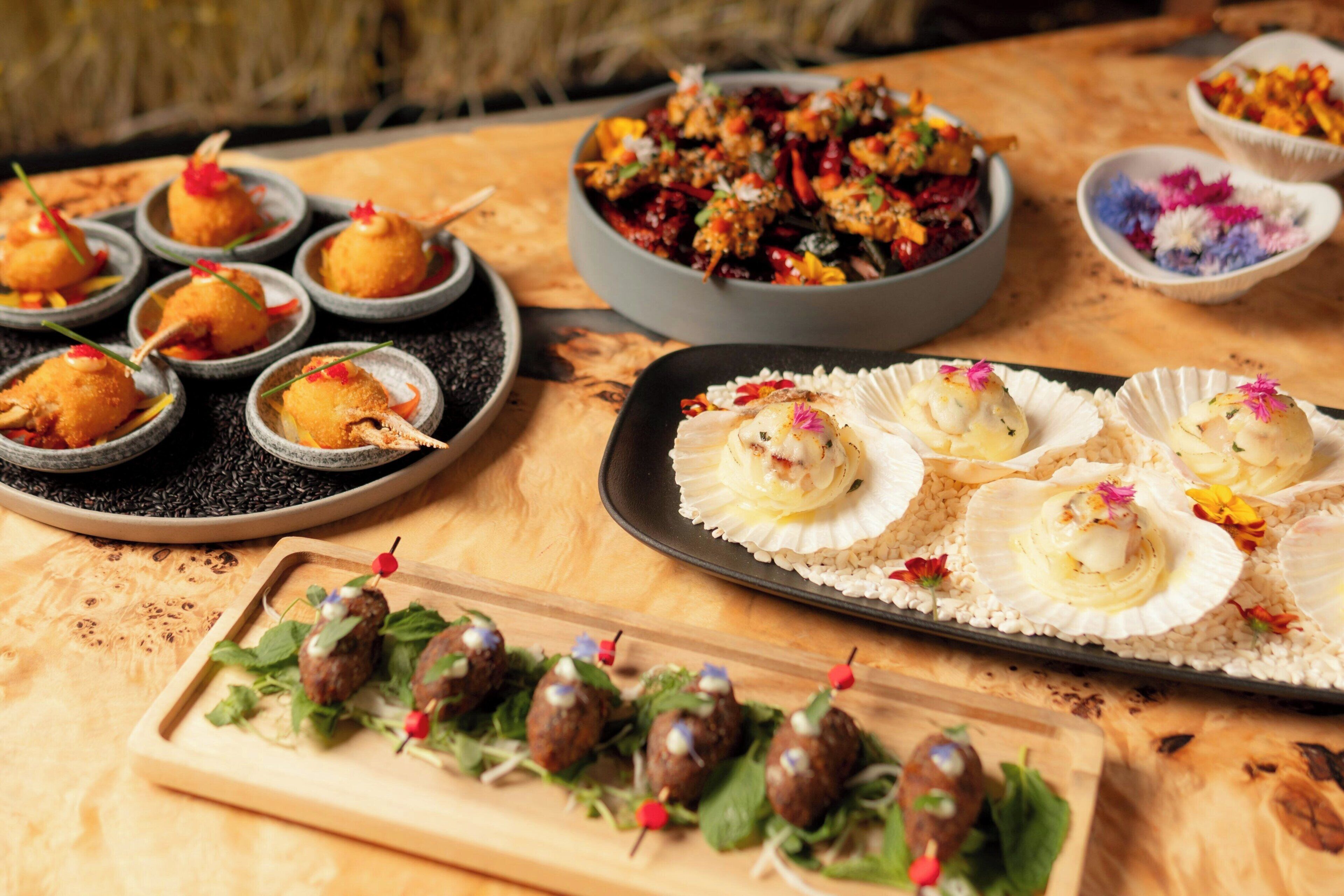 A variety of food items on a wooden table, including appetizers and a bowl of salad.