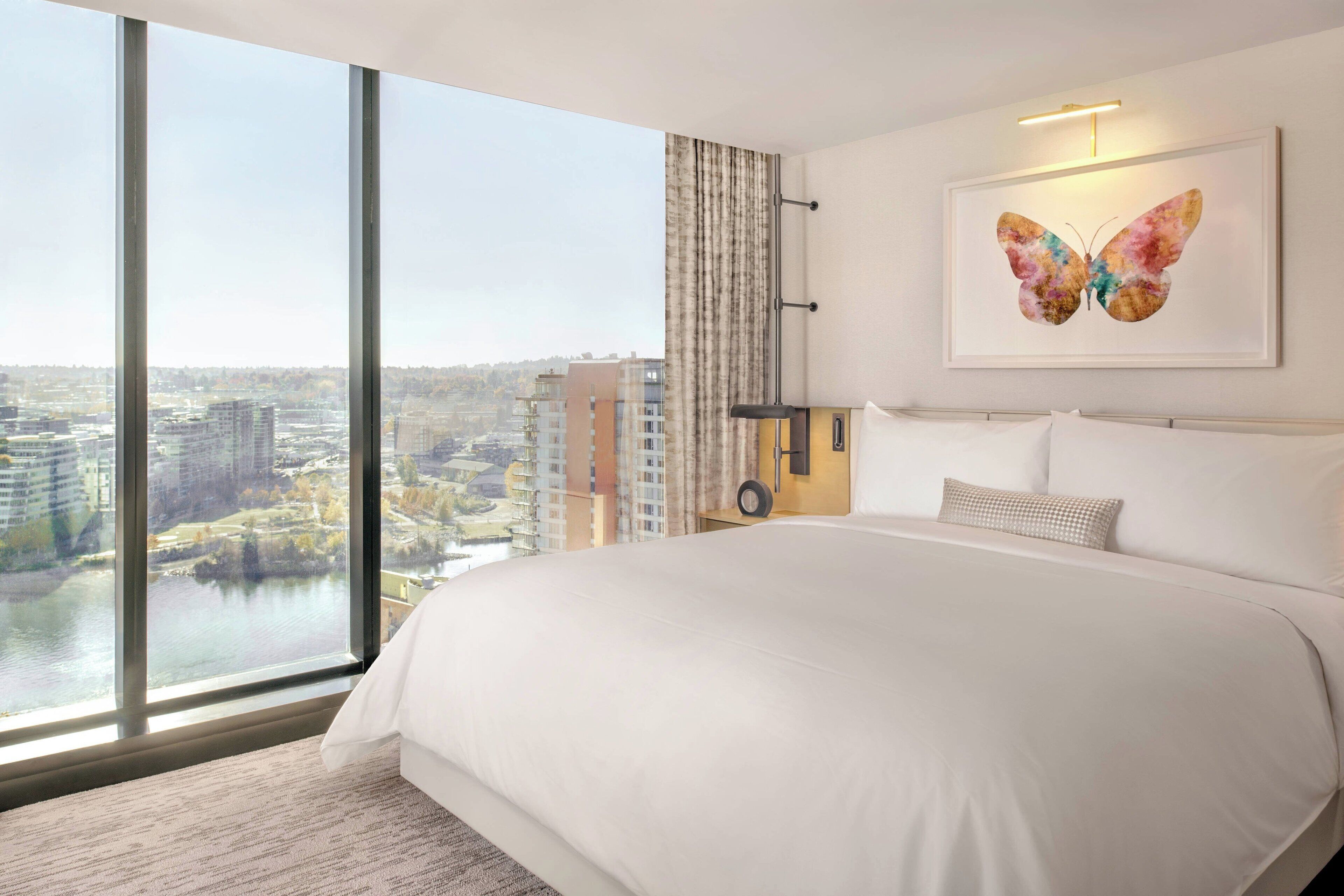 A hotel room with a large bed, a view of the city, and a butterfly artwork on the wall.