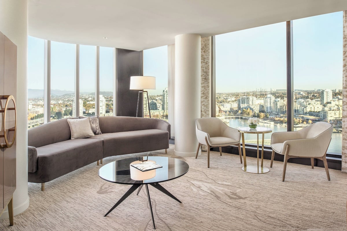 Una sala de estar moderna con un sofá, sillas, una mesa de centro y ventanas amplias con vistas a la ciudad.