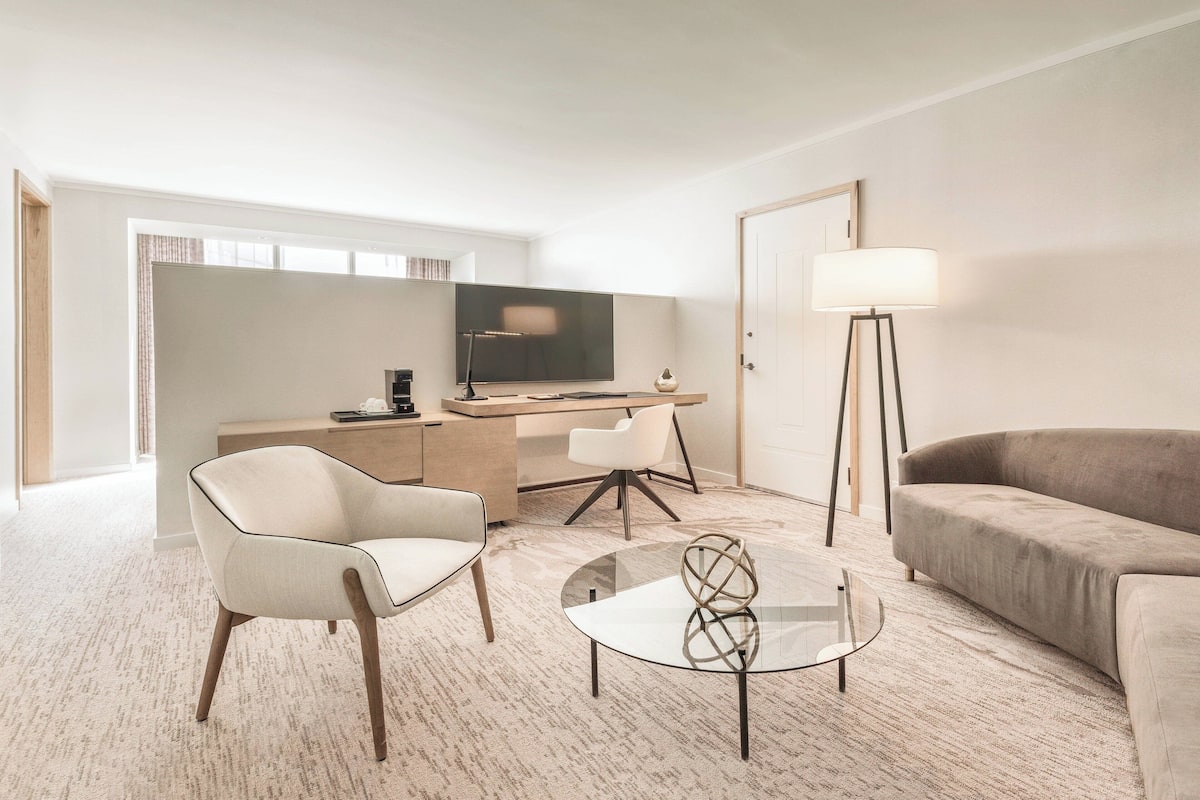 Una habitación de hotel moderna con una cama grande, un escritorio con computadora, una televisión, una silla, un sofá y una lámpara.