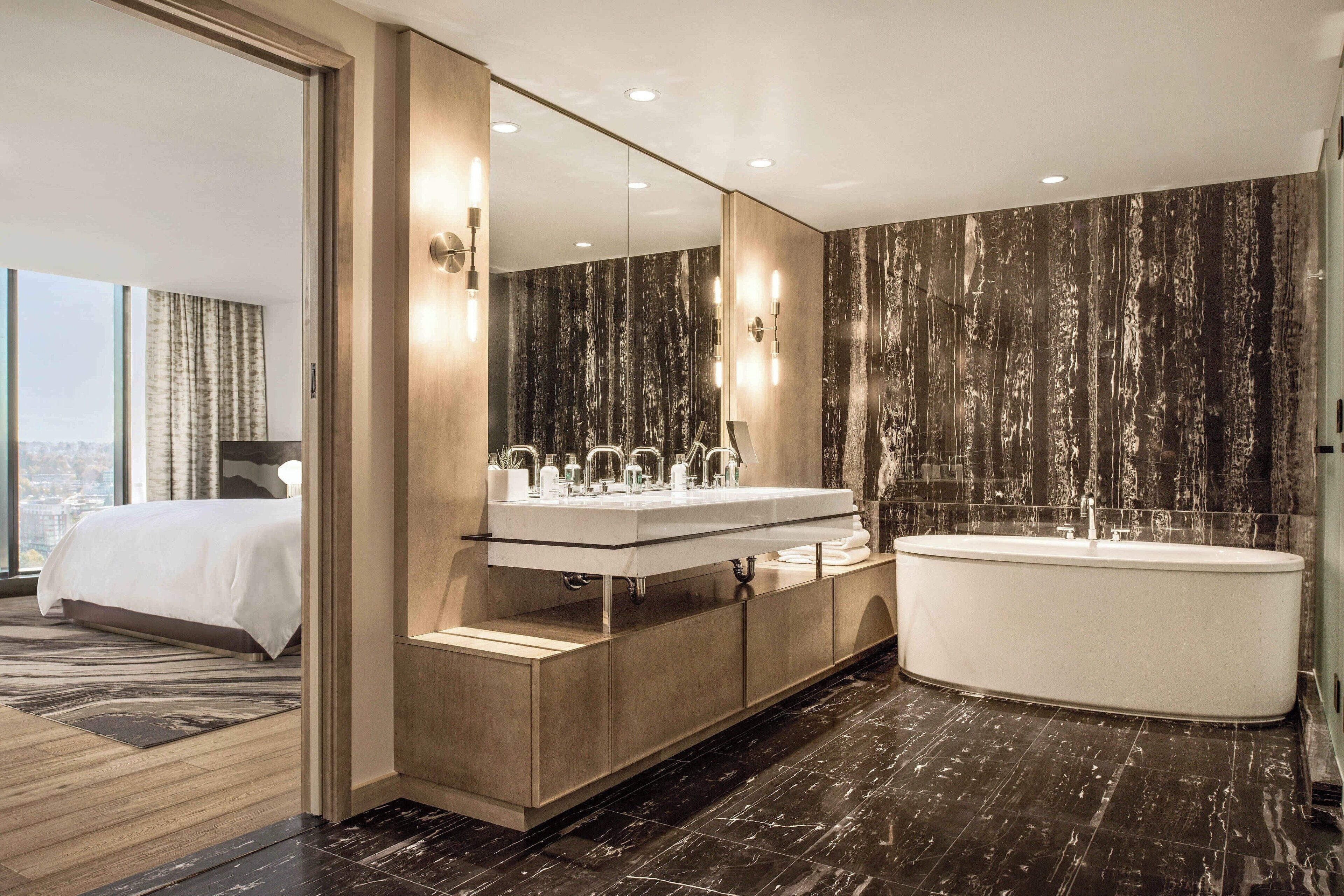 A modern bathroom with a large mirror, two sinks, a bathtub, and a city view.