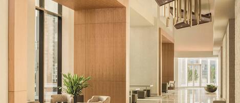A spacious lobby with a high ceiling, a central seating area with chairs and a table, and a large window offering a view of the city.