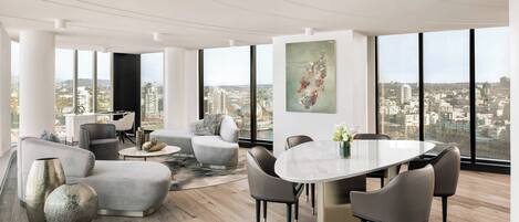 A modern interior with a dining area, sofas, and a large window offering a city view.