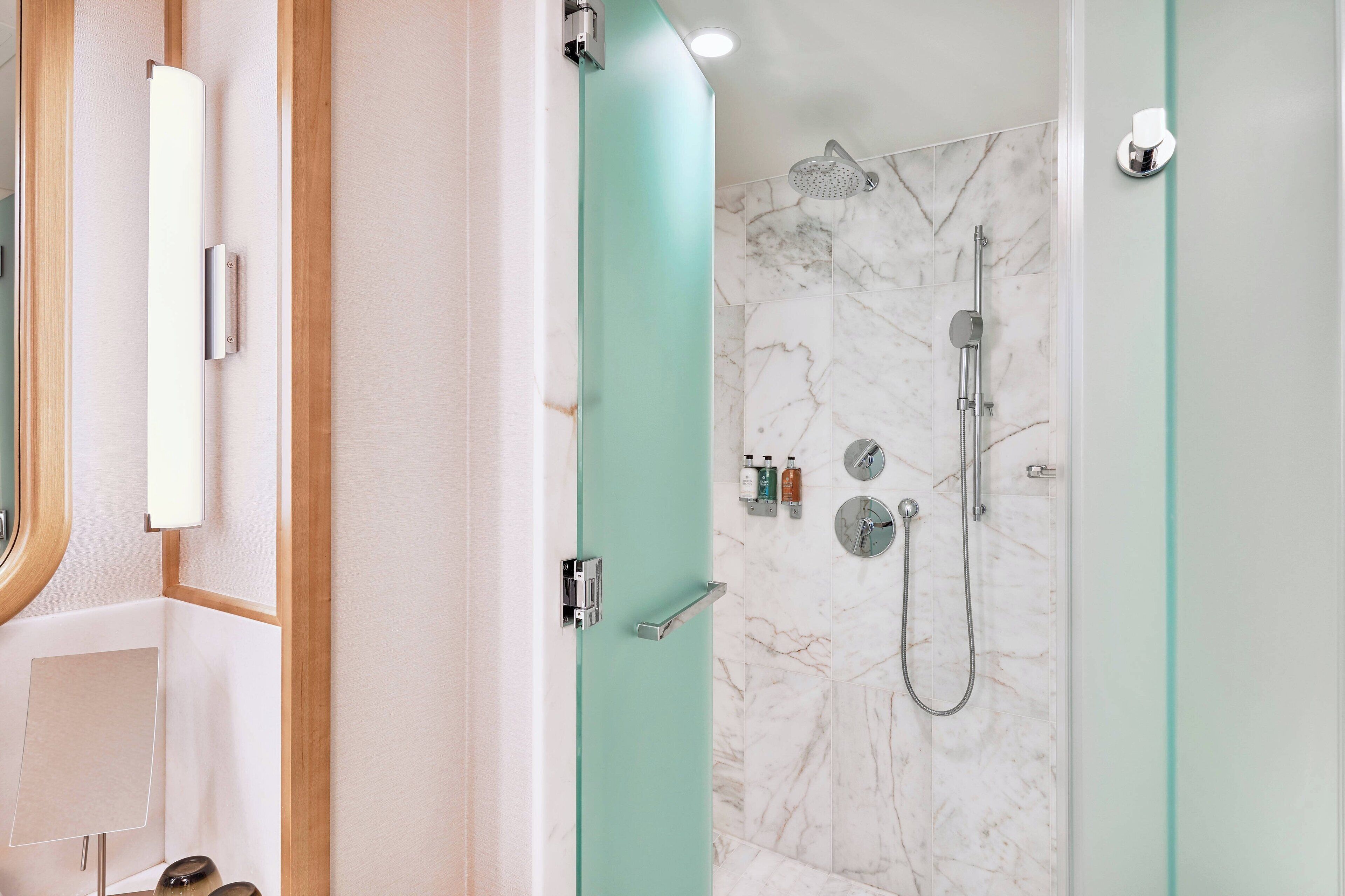 Une salle de bain moderne avec une douche à l’italienne en verre, des carreaux de marbre et une porte en bois.
