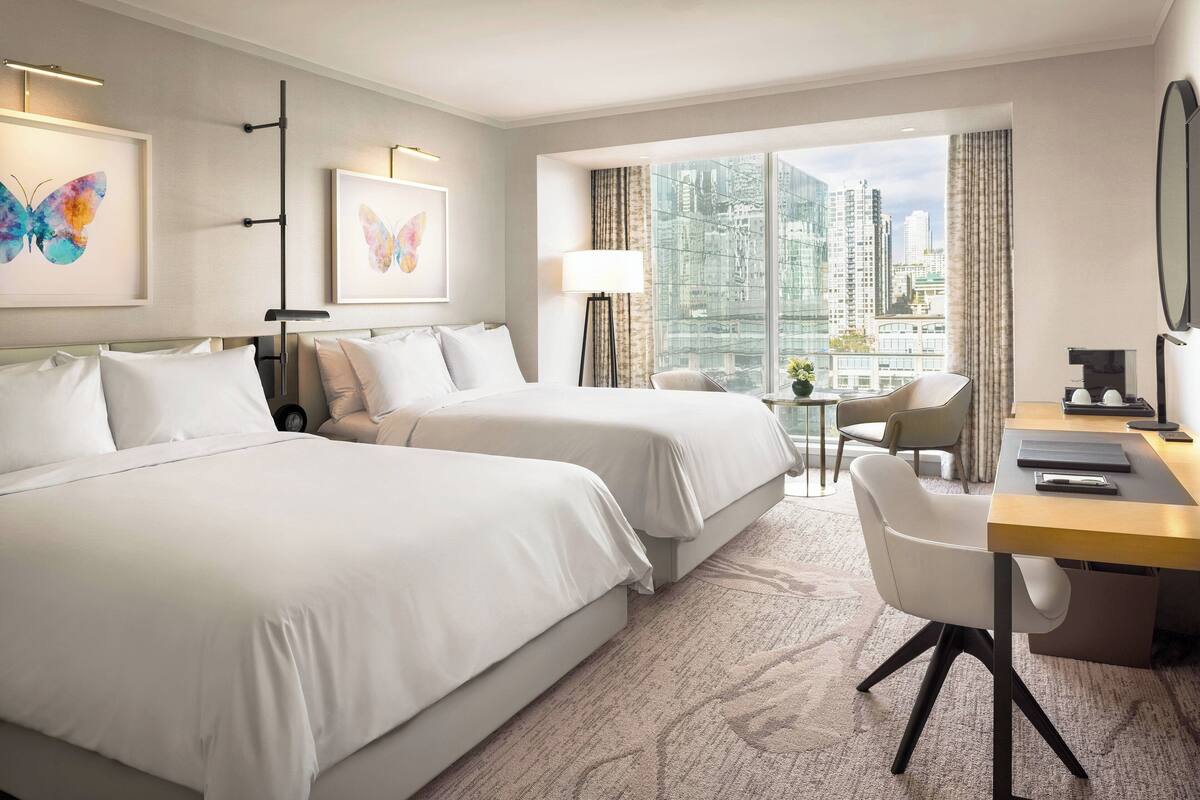 Habitación de hotel con dos camas, un escritorio, una silla y vistas a la ciudad.