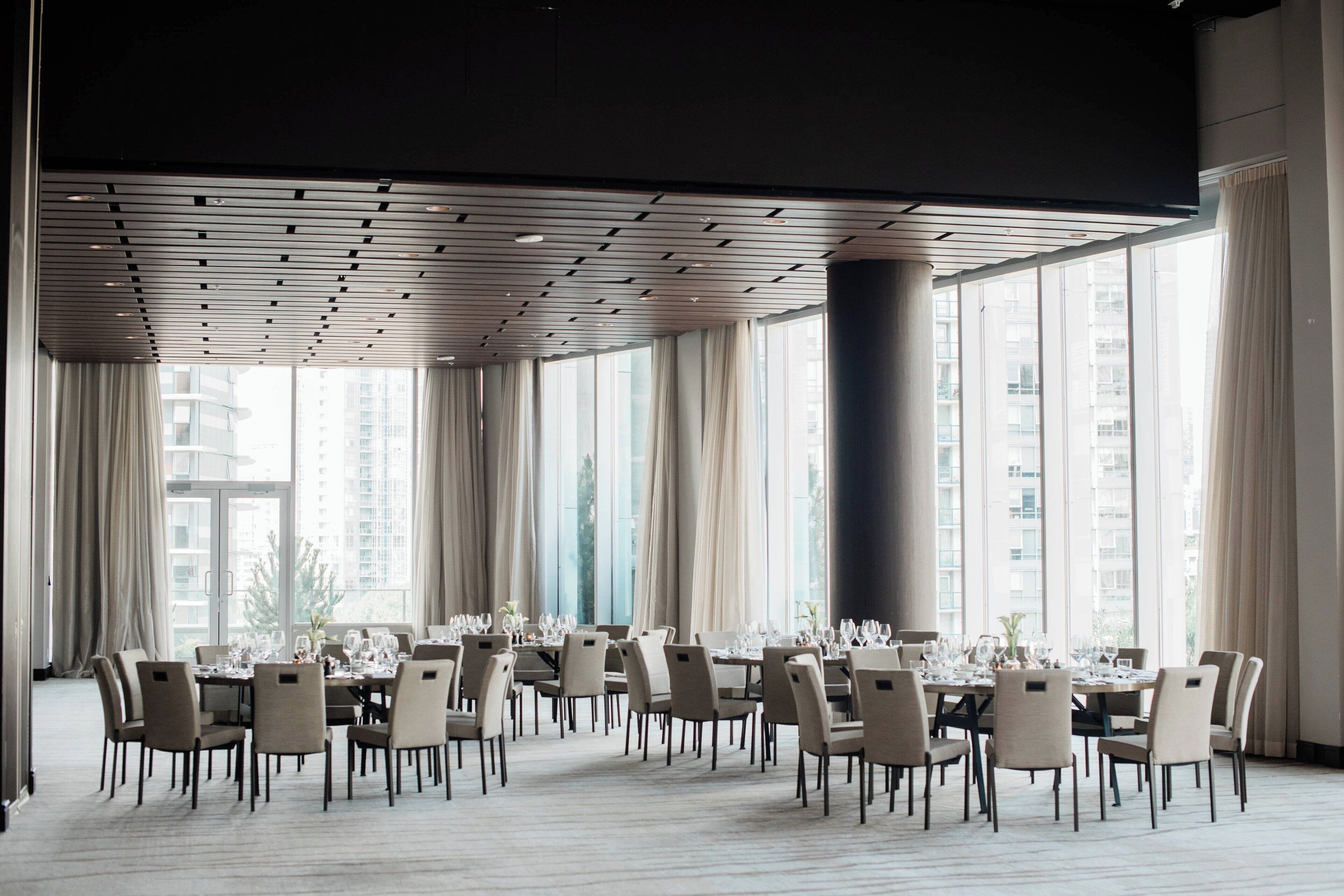 Un vaste espace dédié à la salle à manger, avec plusieurs tables dressées pour le repas, de grandes fenêtres et un design moderne au niveau du plafond.