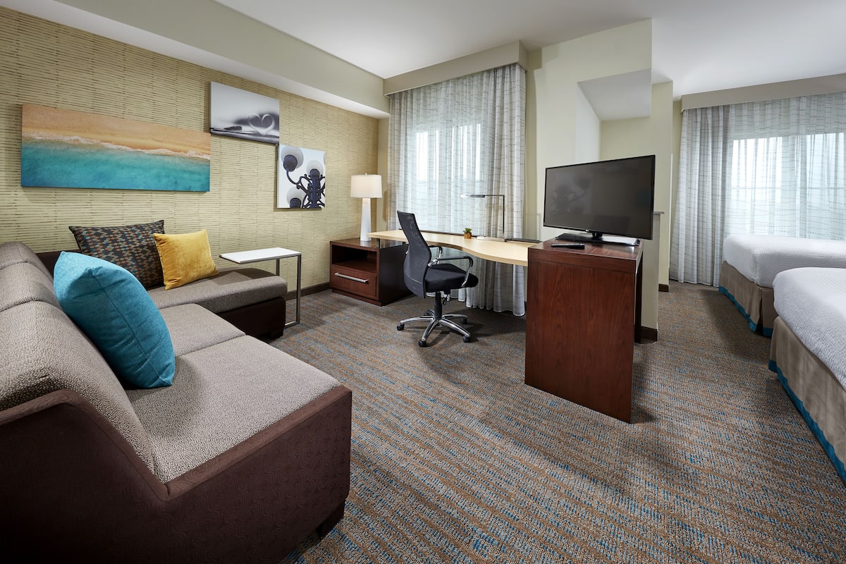 A hotel room with a sofa, a desk, a TV, a bed, and a window with curtains.