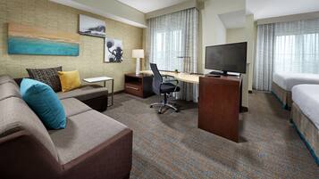 A hotel room with a sofa, a desk, a TV, a bed, and a window with curtains.