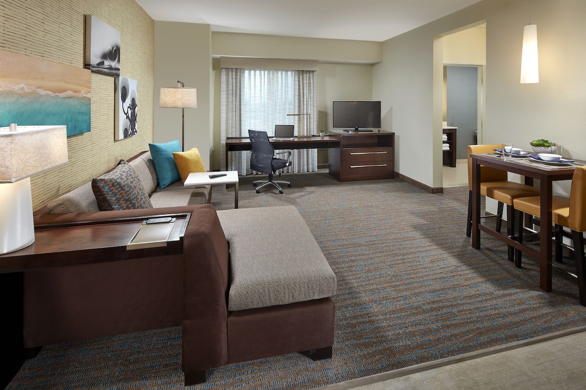 A hotel room with a sofa, desk, TV, and dining area.