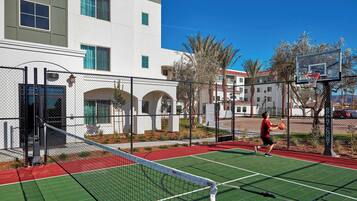 An outdoor basketball court adjacent to a building with a chain-link fence.