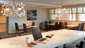 A modern dining area with a long table, chairs, a laptop, a plate of cookies, and a coffee cup.