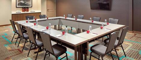 A conference room with a long table, chairs, a television, and a coffee station.