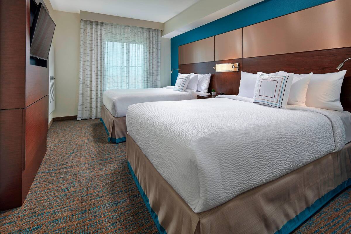 A hotel room with two beds, a TV, and a large window with curtains.