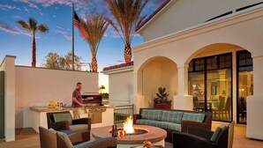 An outdoor patio with wicker furniture, a fire pit, and a grill area.