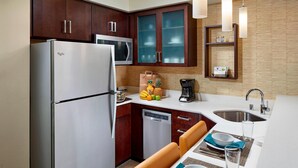 A compact kitchen with a refrigerator, microwave, and dishwasher. There is a dining area with a table set for two, and a coffee maker on the counter.