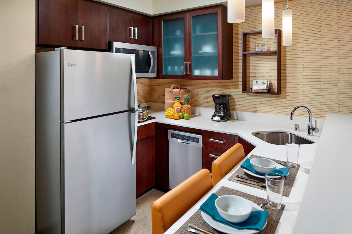 A compact kitchen with a refrigerator, microwave, and dishwasher. There is a dining area with a table set for two, and a coffee maker on the counter.