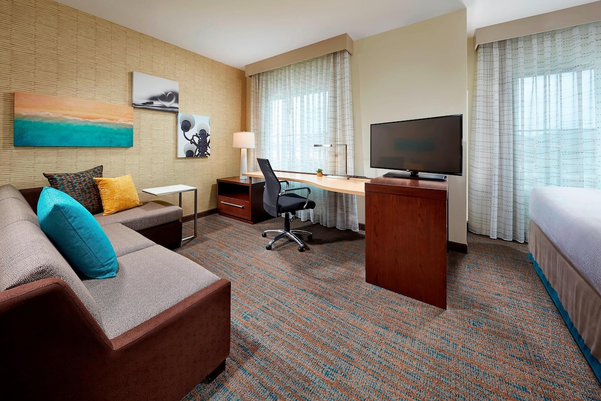 A hotel room with a sofa, desk, TV, and a bed.