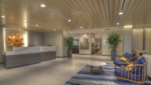 A modern reception area with a wooden ceiling, a reception desk, a seating area with blue and yellow upholstered chairs, and a large abstract artwork on the wall.