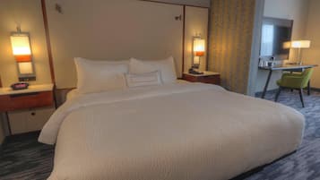 A hotel room with a large bed, two bedside tables with lamps, a desk with a chair, and a mirror.