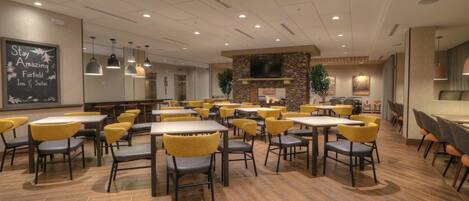 A spacious dining area with multiple tables and chairs, a stone fireplace, and a television mounted on the wall.