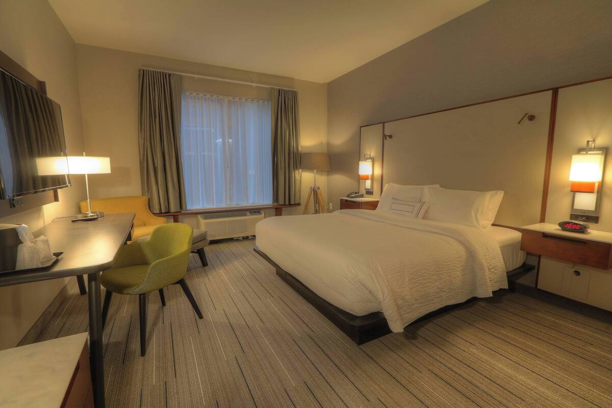 Une chambre d’hôtel avec un lit, un bureau et une chaise, une télévision et une fenêtre avec des rideaux.