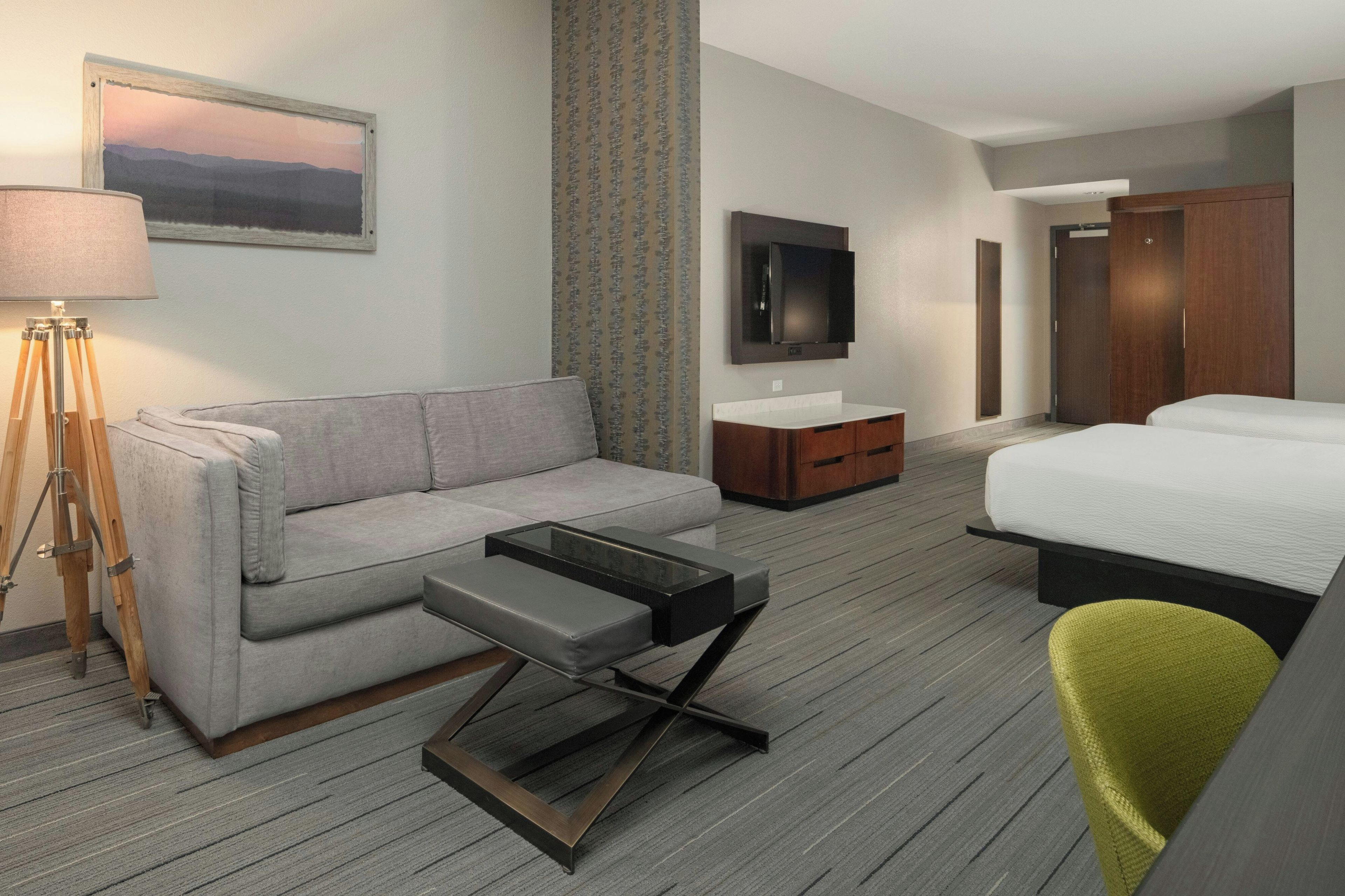 Une chambre d’hôtel avec un canapé, une petite table, une télévision, une armoire et un lit.