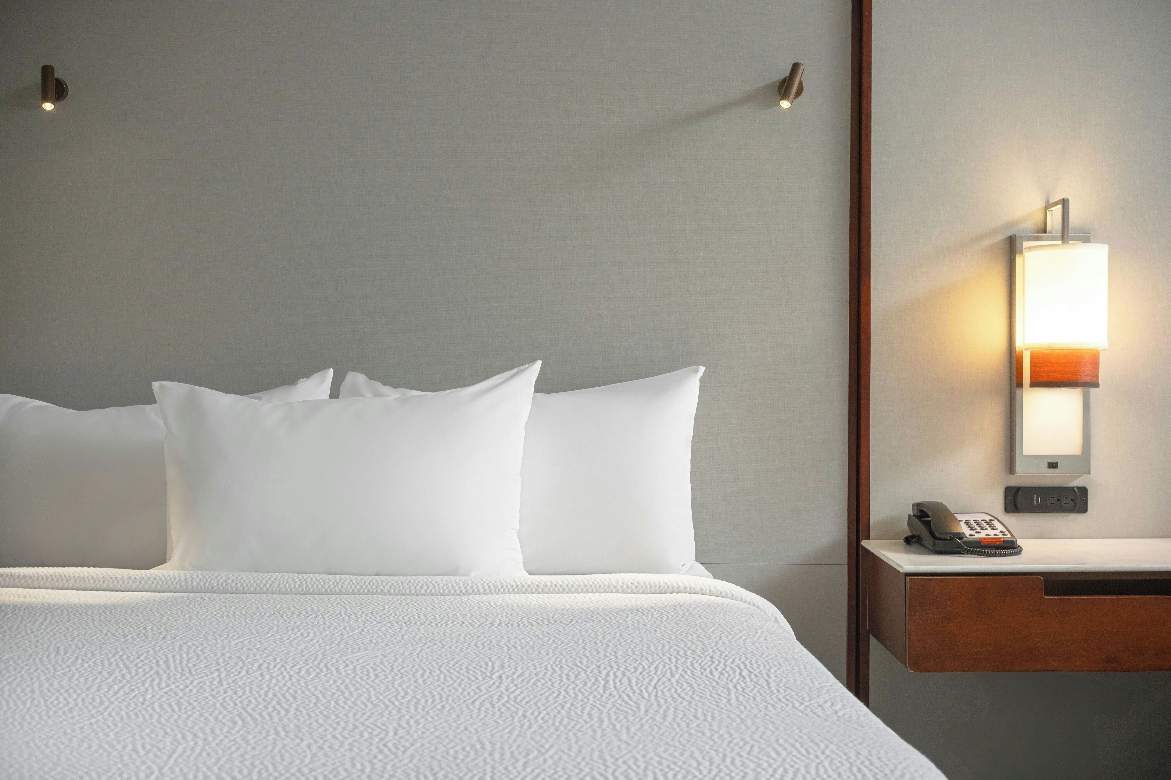 Une chambre d’hôtel avec un lit, des oreillers, une table de chevet avec une lampe et un téléphone.