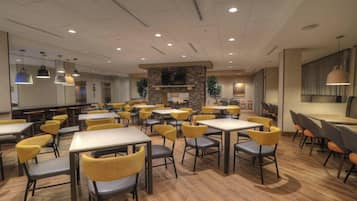 A spacious dining area with multiple tables and chairs, a stone fireplace, and a television mounted on the wall.