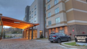A Fairfield Inn & Suites Marriott hotel entrance with a covered walkway, brick pathway, and a parked SUV.