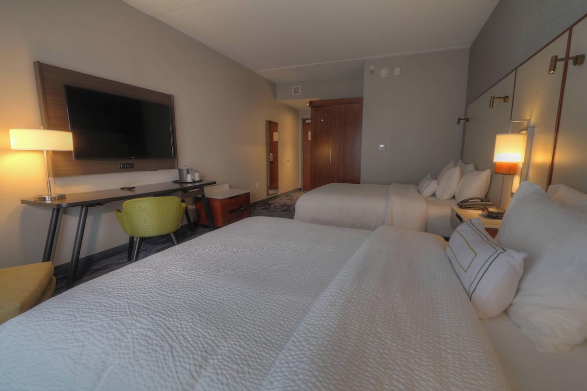 Une chambre d’hôtel avec deux lits, un bureau doté d’un téléviseur à écran plat, une chaise et une table de chevet avec des lampes.