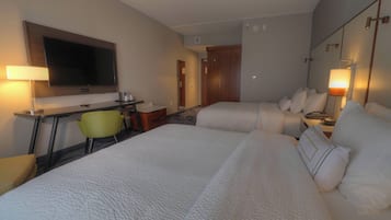 Habitación de hotel con dos camas, un escritorio, un televisor de pantalla plana, una silla y una mesita de noche con lámparas.