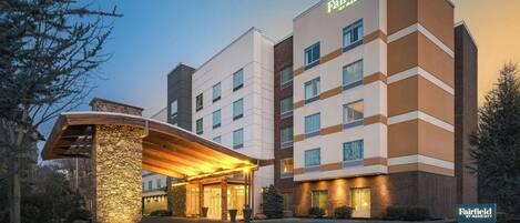 Um hotel Fairfield by Marriott com design moderno, destacando uma entrada imponente com galeria coberta e fachada em pedra.