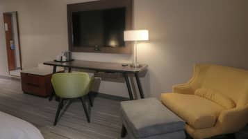 A hotel room with a bed, a desk with a chair, a television, and a lamp.