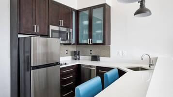 Una cocina moderna con armarios de madera oscura, electrodomésticos de acero inoxidable, encimera blanca y taburetes de bar azules.