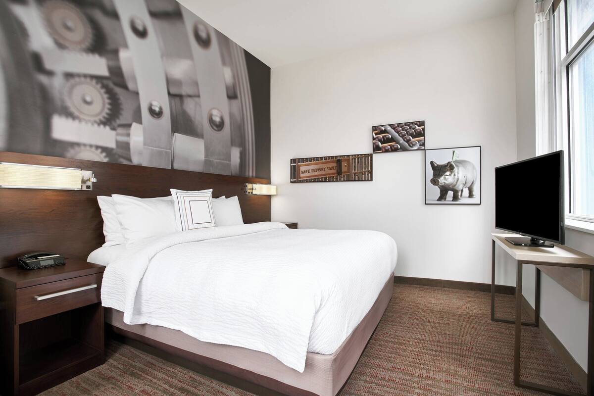 Een hotelkamer met een bed, nachtkastje, bureau en televisie.