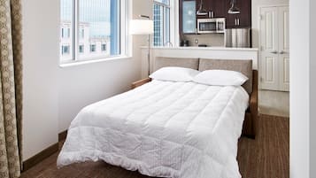 A hotel room with a large bed, a kitchenette, and a view of the city through the window.
