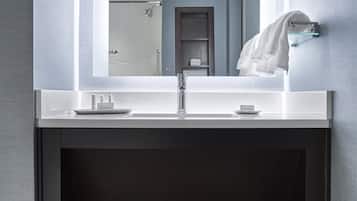 A modern bathroom with a large mirror, white countertop, and dark cabinetry.