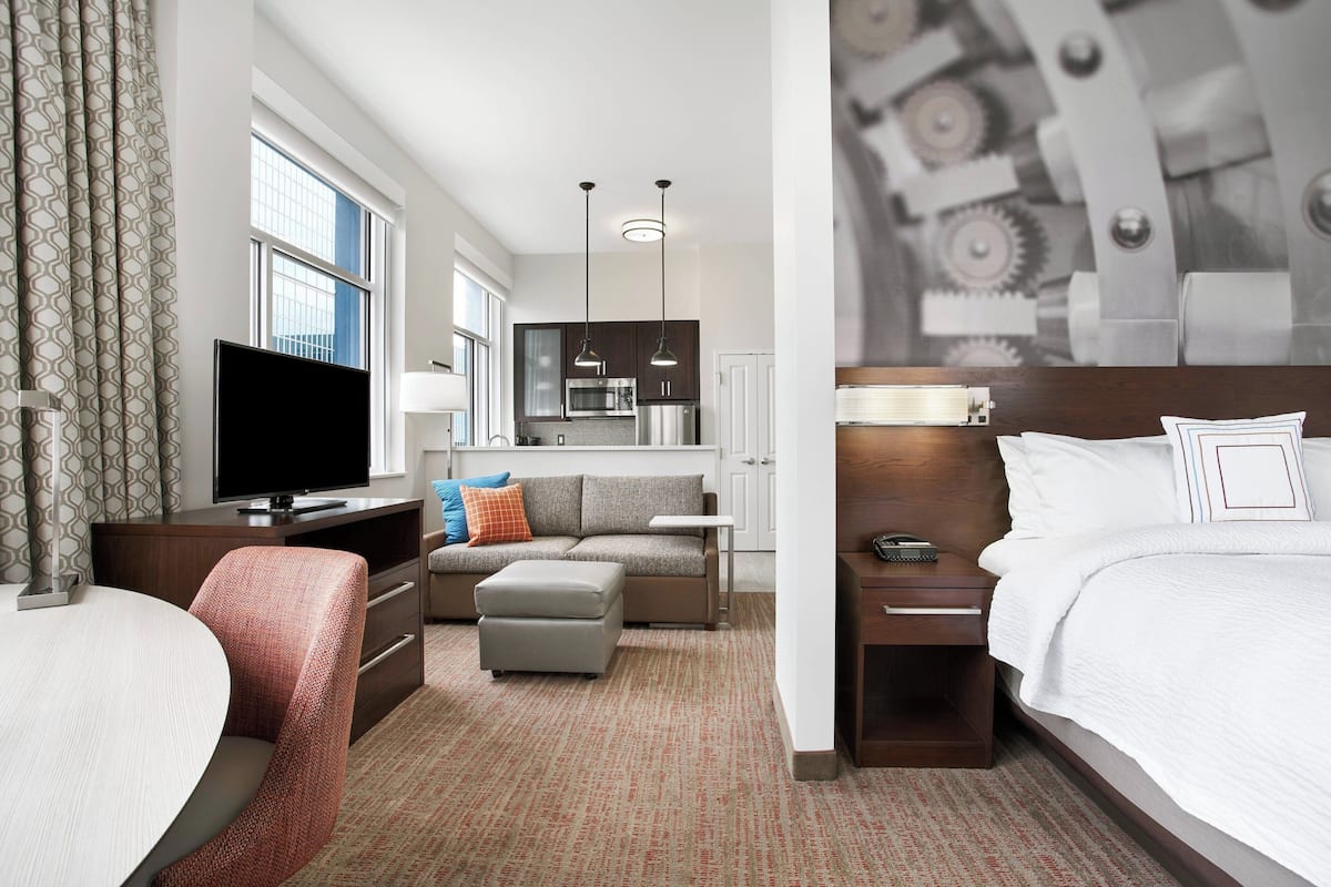 Een hotelkamer met een televisie, bank, voetenbankje en een bed.