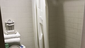Ein Badezimmer mit Toilette, einer Duschkabine mit Vorhang und einem Stapel weißer Handtücher.