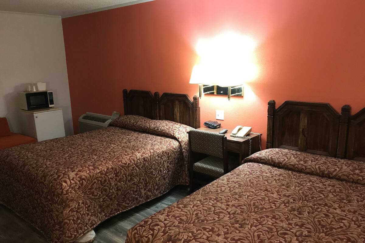 Habitación de hotel con dos camas, un escritorio con lámpara, teléfono y televisor sobre una mesita.